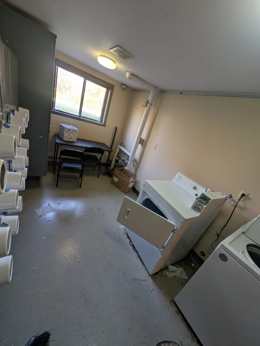 Shared apartment laundry room in Fargo, ND before commercial cleaning, showing dirty floors and debris scattered around the laundry machines
